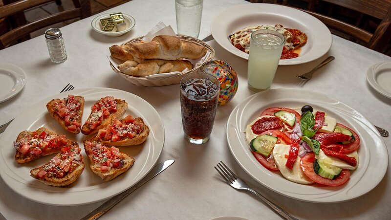 Three plated appetizers with drinks and basket of bread